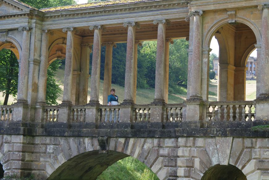 woman in regency dress looking over the side of a bridge